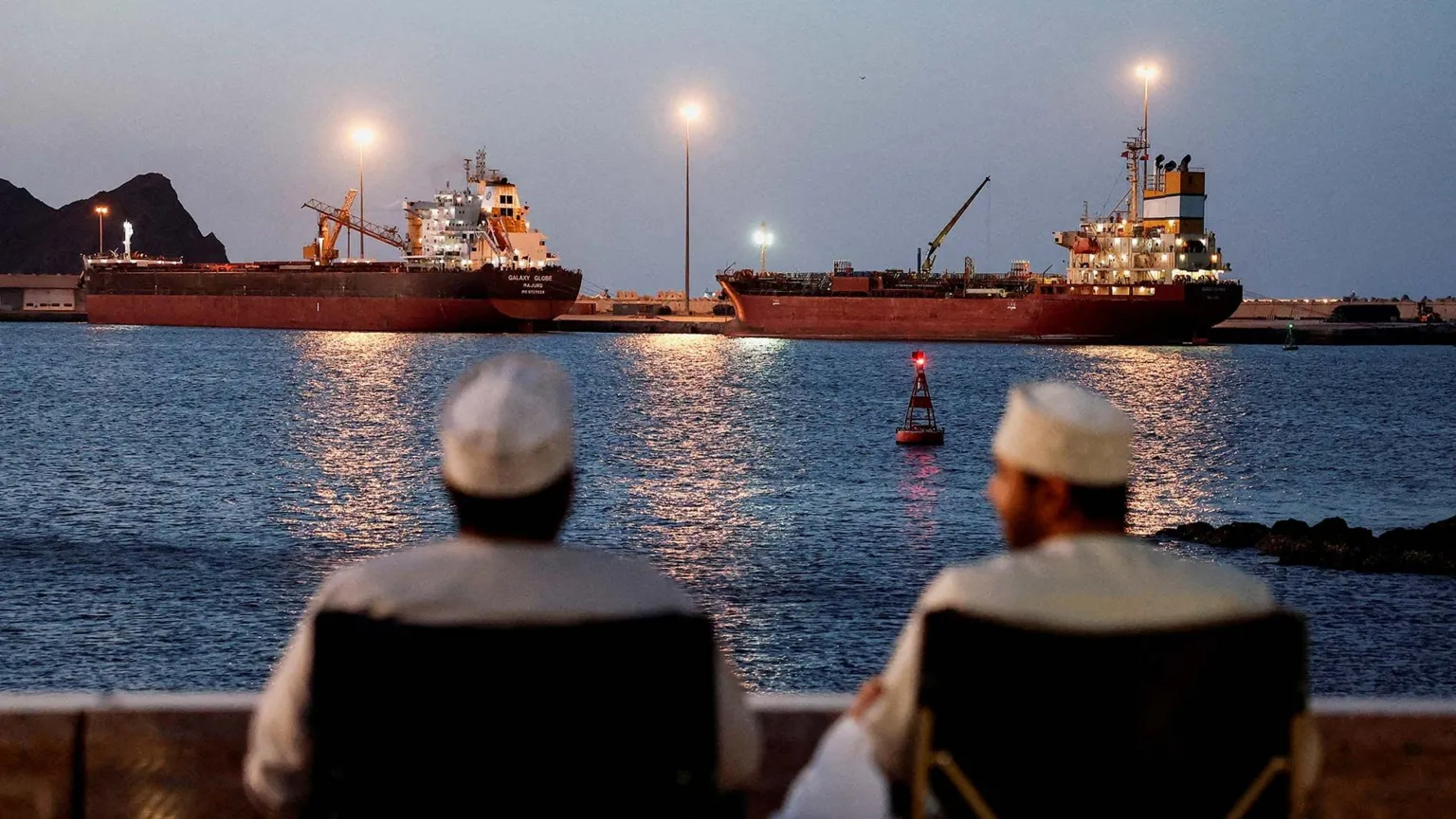 Crew members aboard a stranded vessel observe the Galaxy Globe bulk carrier and other ships trapped in the Strait of Hormuz.