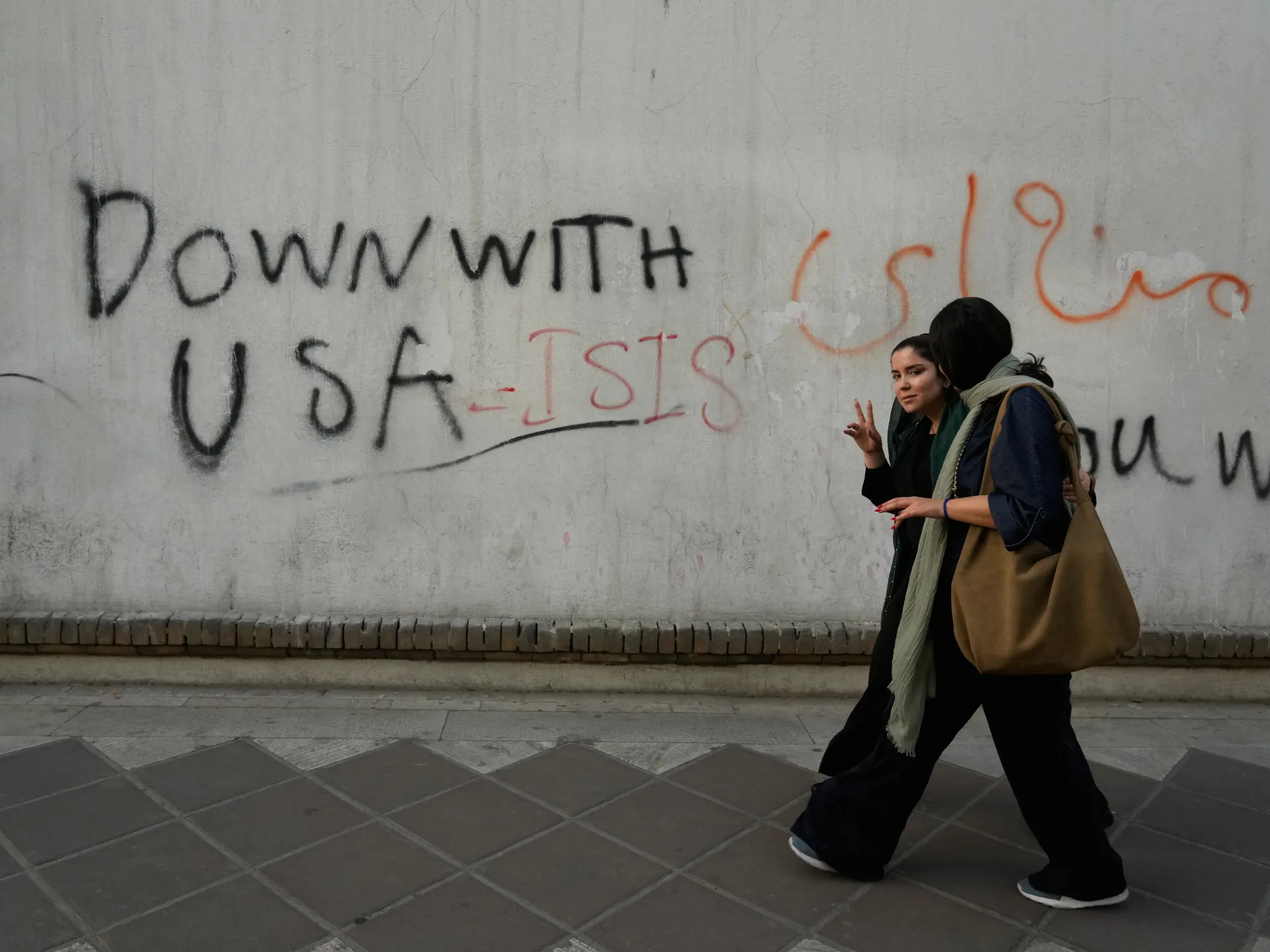 A woman reacts to the camera as she walks past anti-US graffiti painted on the wall of the British Embassy in Tehran, Iran, Saturday, June 6, 2026 [Vahid Salemi/AP Photo]