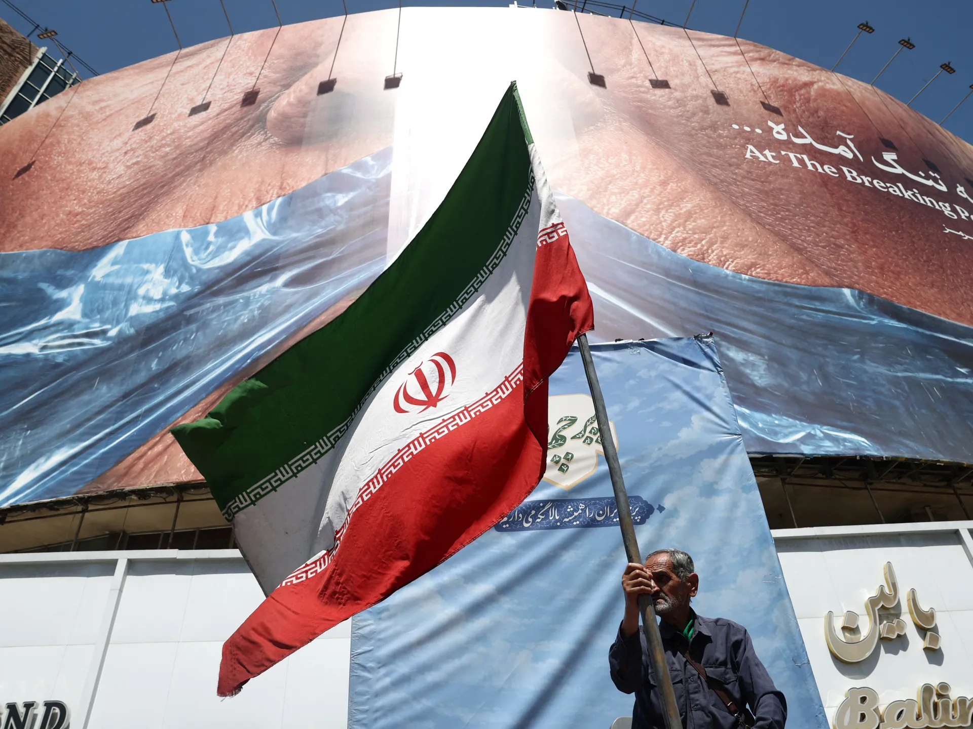 A man holds an Iranian flag near an anti-US billboard depicting US President Donald Trump and the Strait of Hormuz, in Tehran, Iran, May 30, 2026 [Majid Asgaripour/WANA (West Asia News Agency) via Reuters]