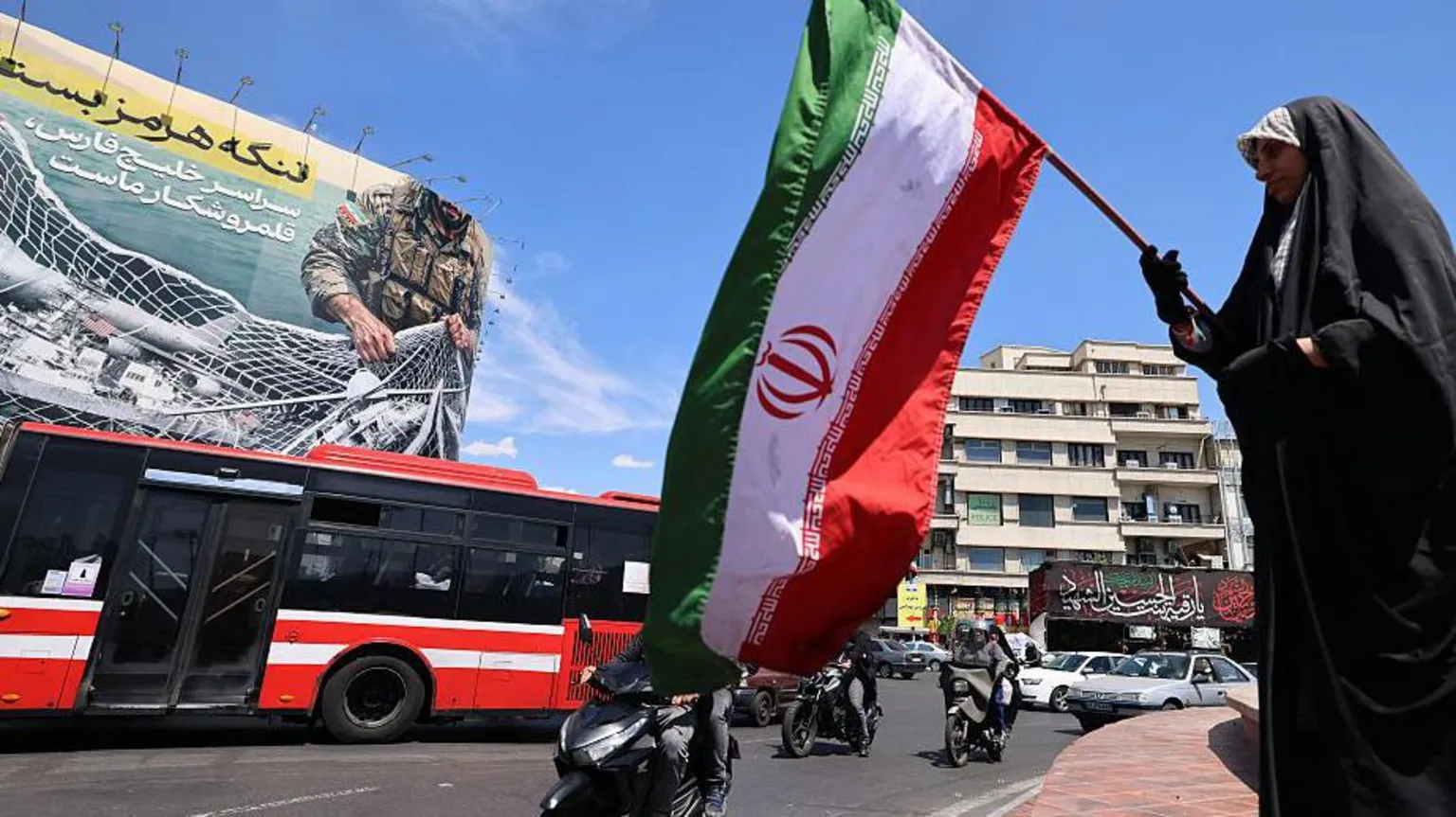 A woman waves Iran's national flag in front of a giant billboard reading 'The Strait of Hormuz remains closed' at the Revolution Square in Tehran on 12 April