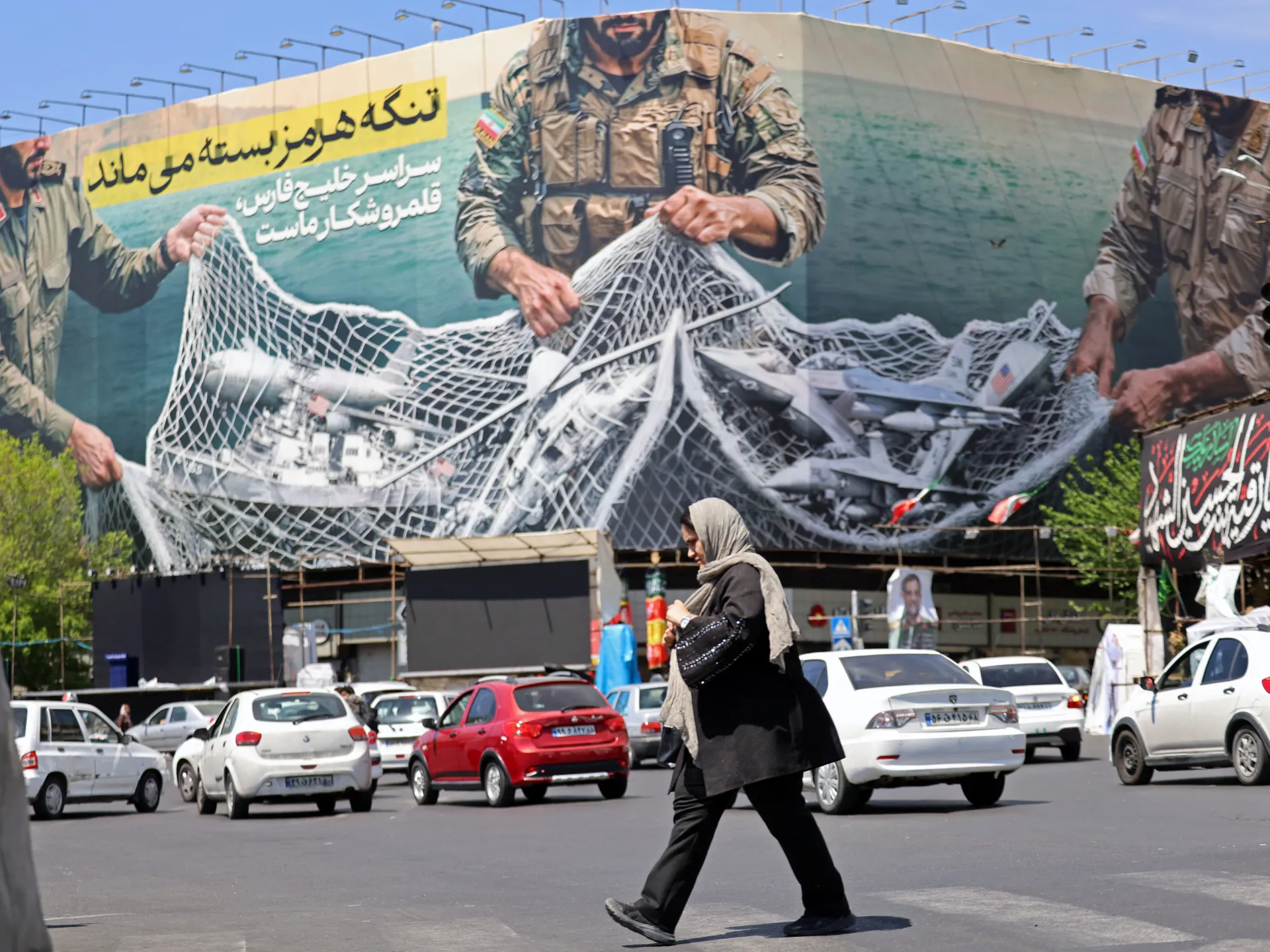 A woman walks past a giant billboard reading 'The Strait of Hormuz remains closed' at the Revolution Square in Tehran [Atta Kenare/AFP]