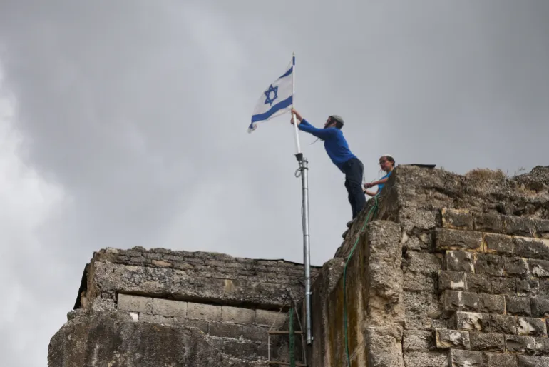 Israeli settlers place a flag atop a building during the re-establishment of Sa-Nur settlement, evacuated nearly 21 years ago.