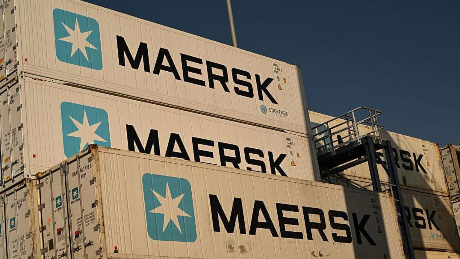 Shipping containers stacked at port as Strait of Hormuz closure adds hundreds of millions in monthly costs.